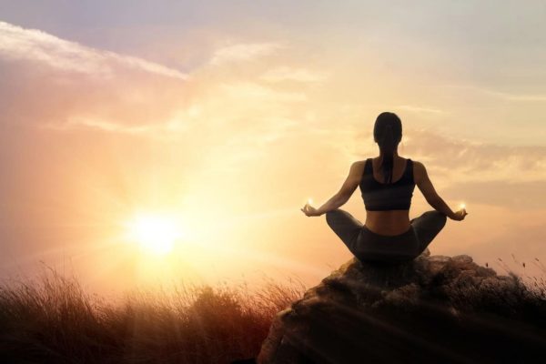 Woman practices meditating yoga at is an asana on a stone, sunset mountains background